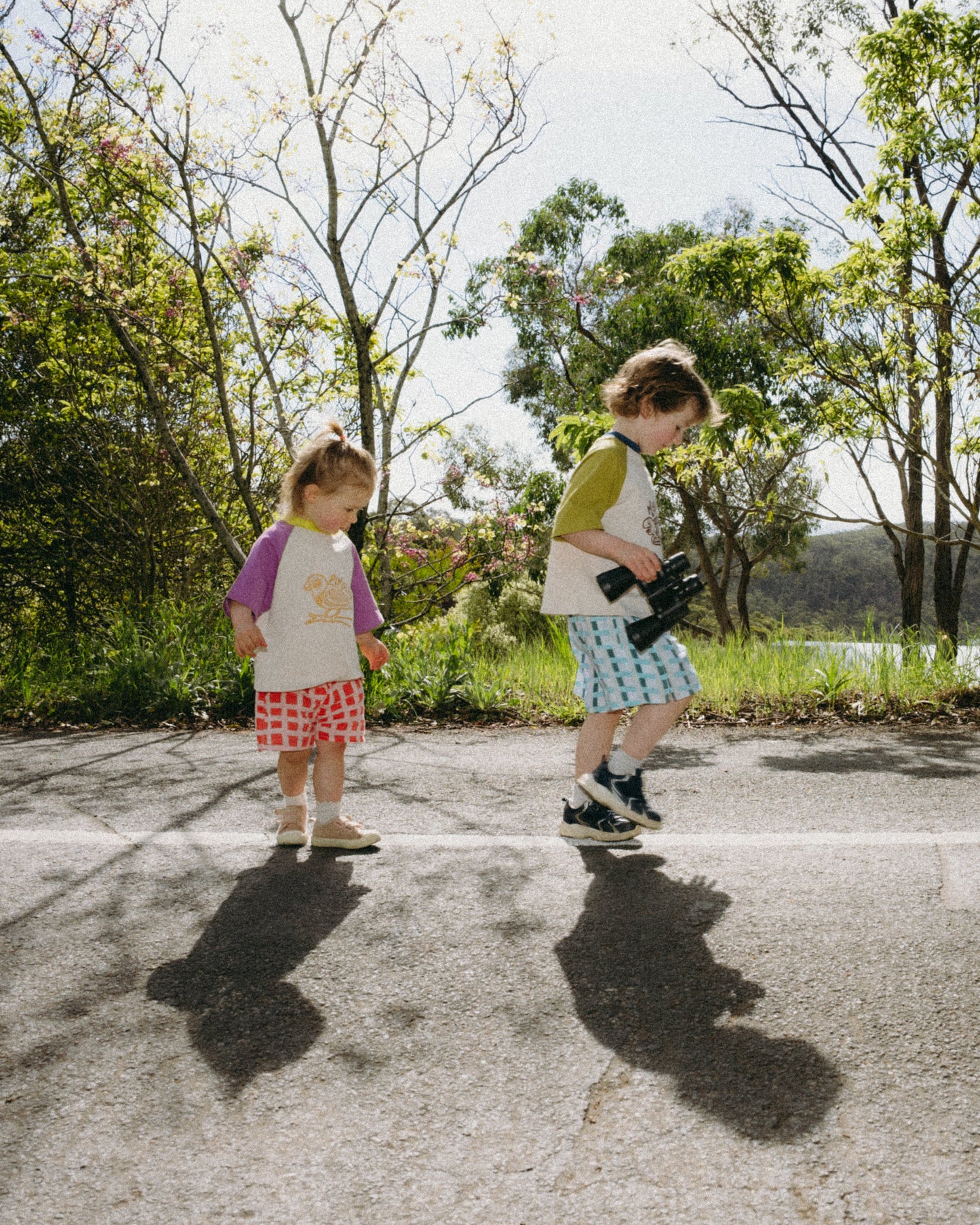 Two children standing on a paved path with trees in the background