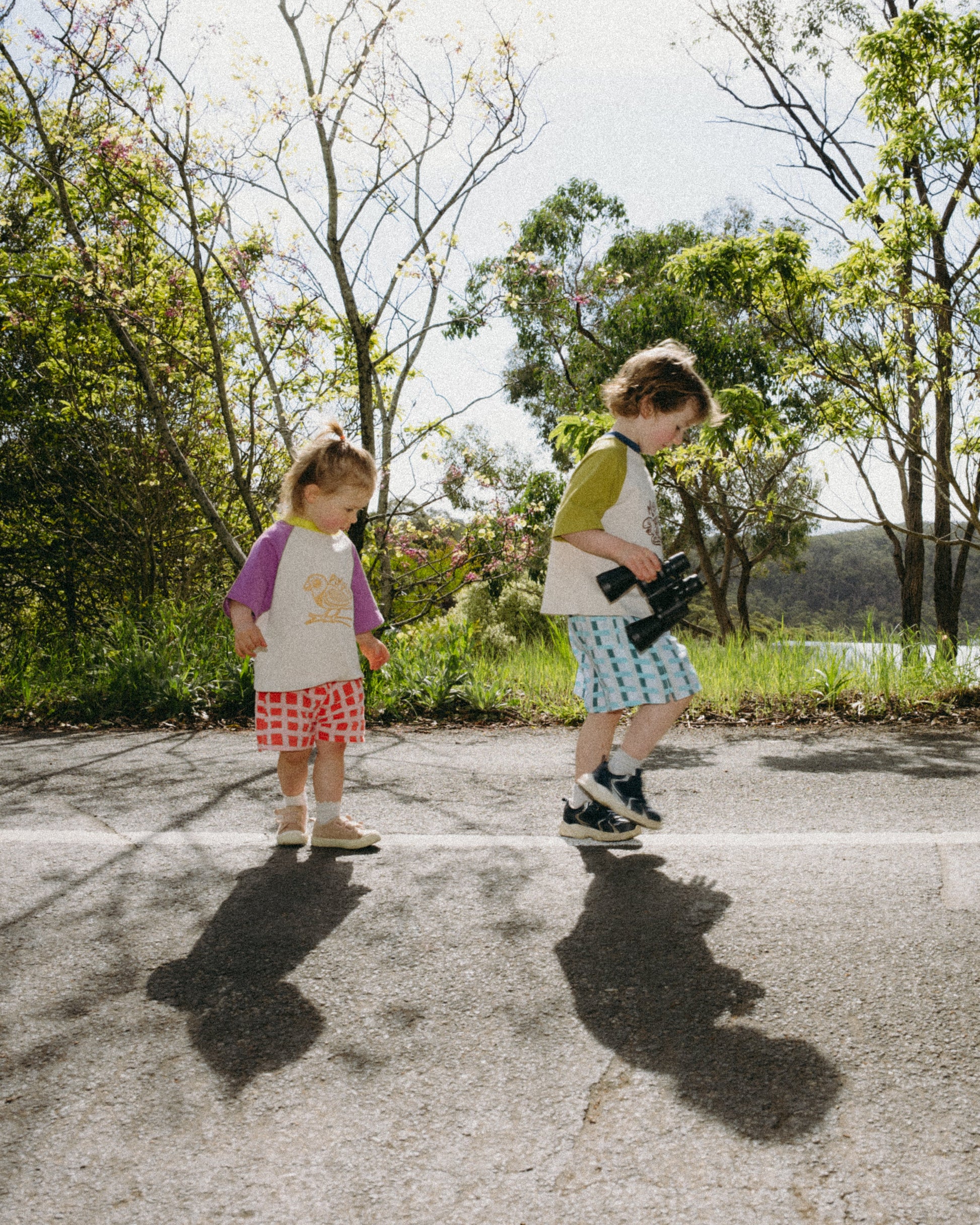 Two children standing on a paved path with trees in the background